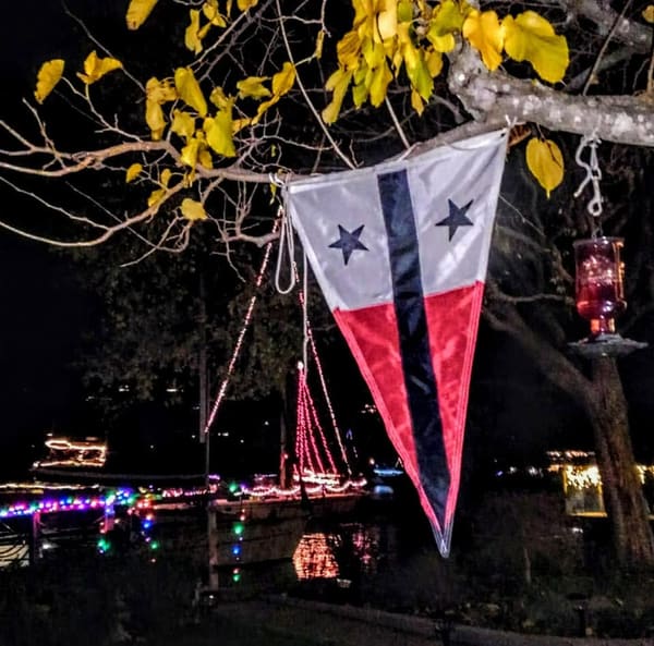 A Hidden Harbor Yacht Club burgee being displayed with a lighted boat parade in the background