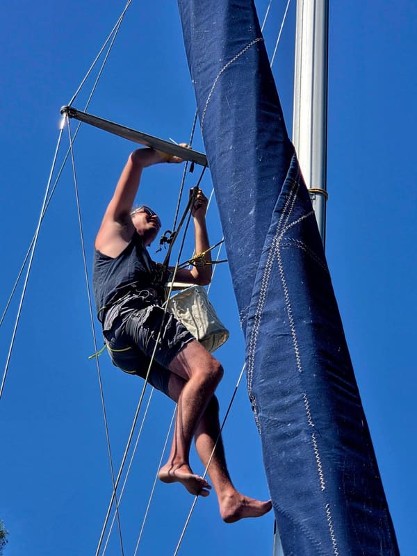 A man making repairs to a sailboat mast while seated in a bosun's chair