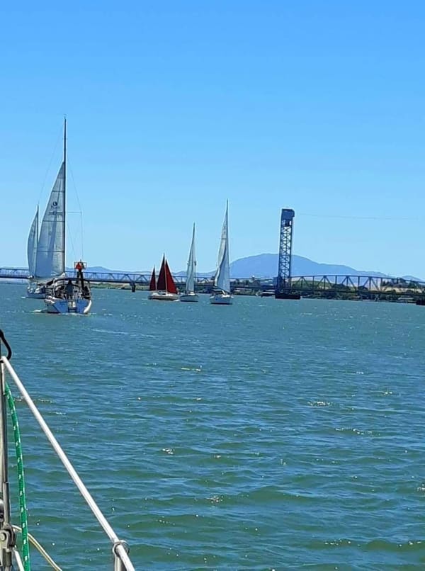 Five sailboats with sails up on calm water waiting for a drawbridge to open