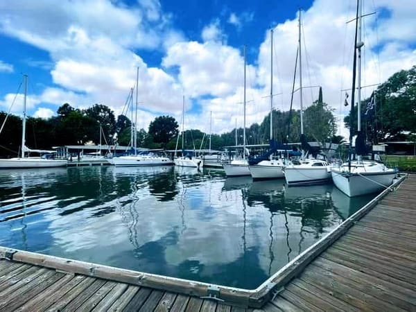 Sailboats docked at a marina lined up against a blue sky with clouds
